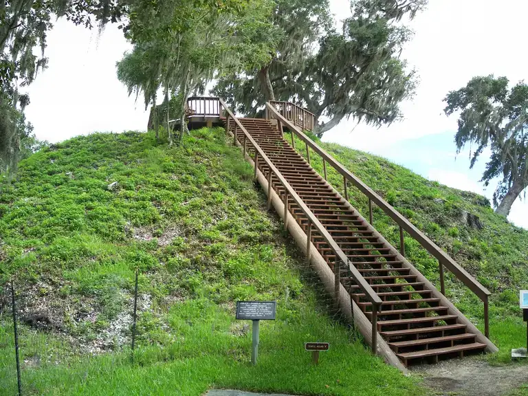 Wooden staircase climbing the grassy Temple Mound at Crystal River Archaeological State Park, shaded by moss-draped oaks